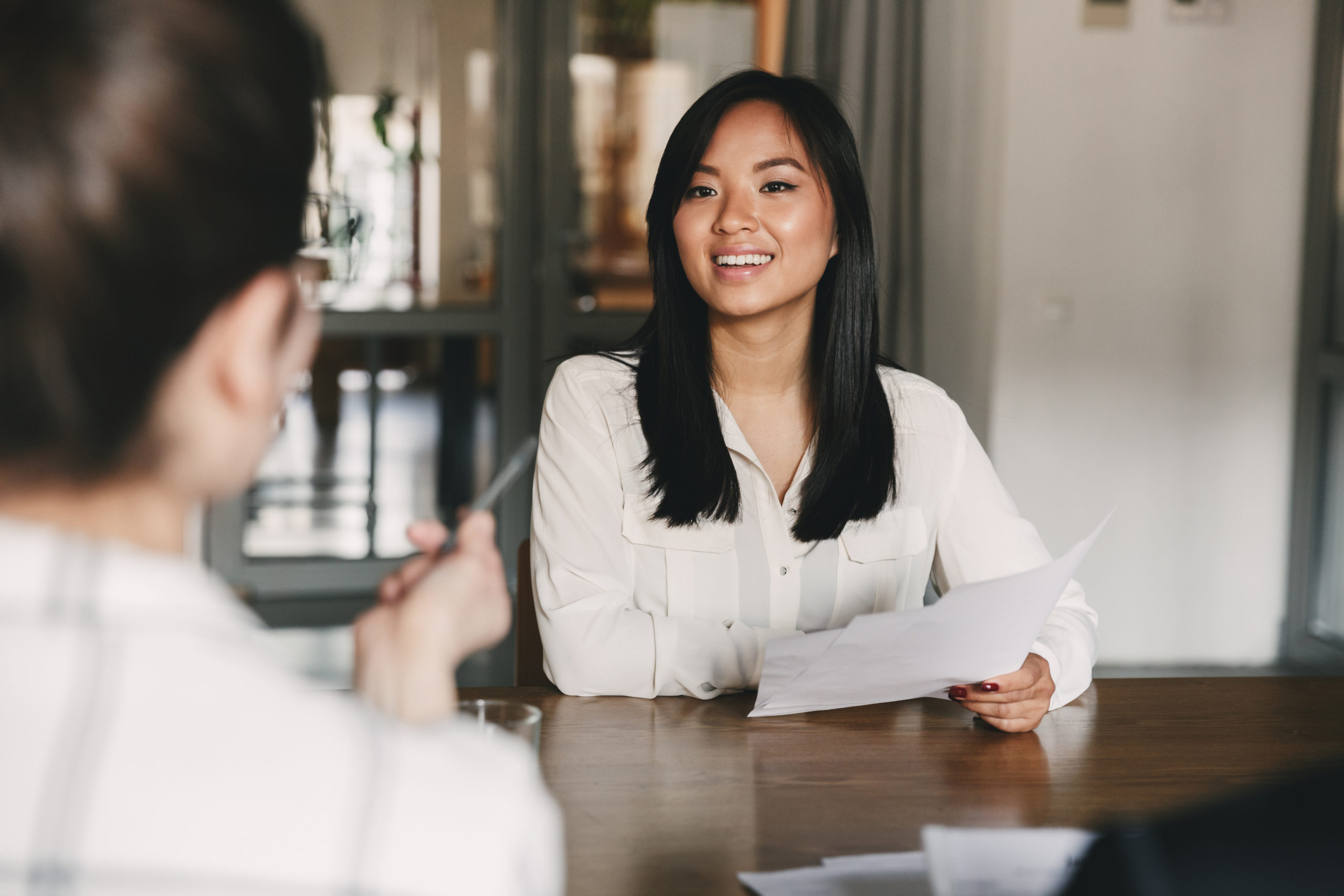 Business, career and placement concept - joyful asian woman smiling and holding resume while sitting in front of directors during corporate meeting or job interview